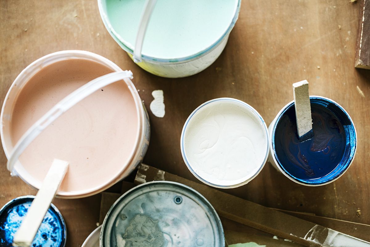 Four open paint cans and two corresponding lids viewed from above. The colors include pink, white, navy blue, and powder blue.