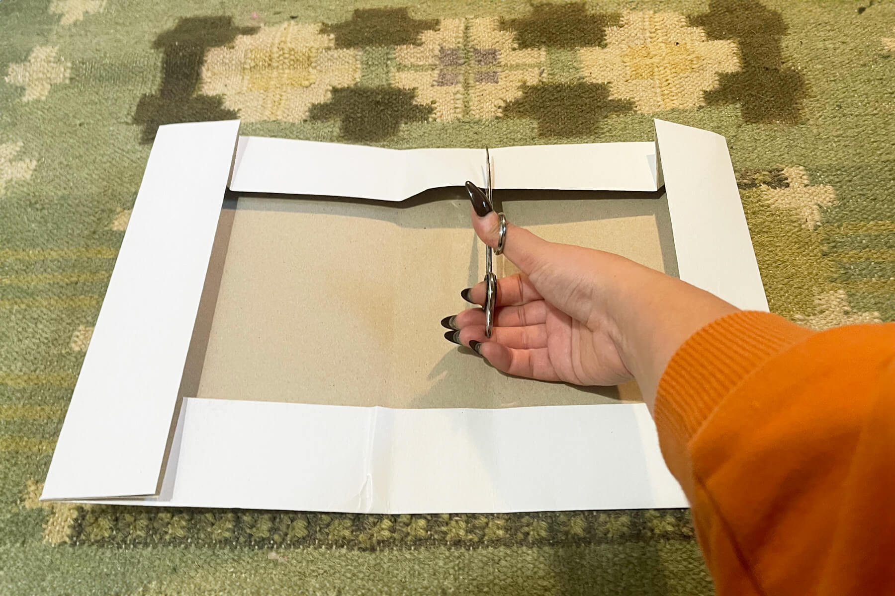 Anonymous person using scissors to cut slits in a shirt box in order to make it smaller.