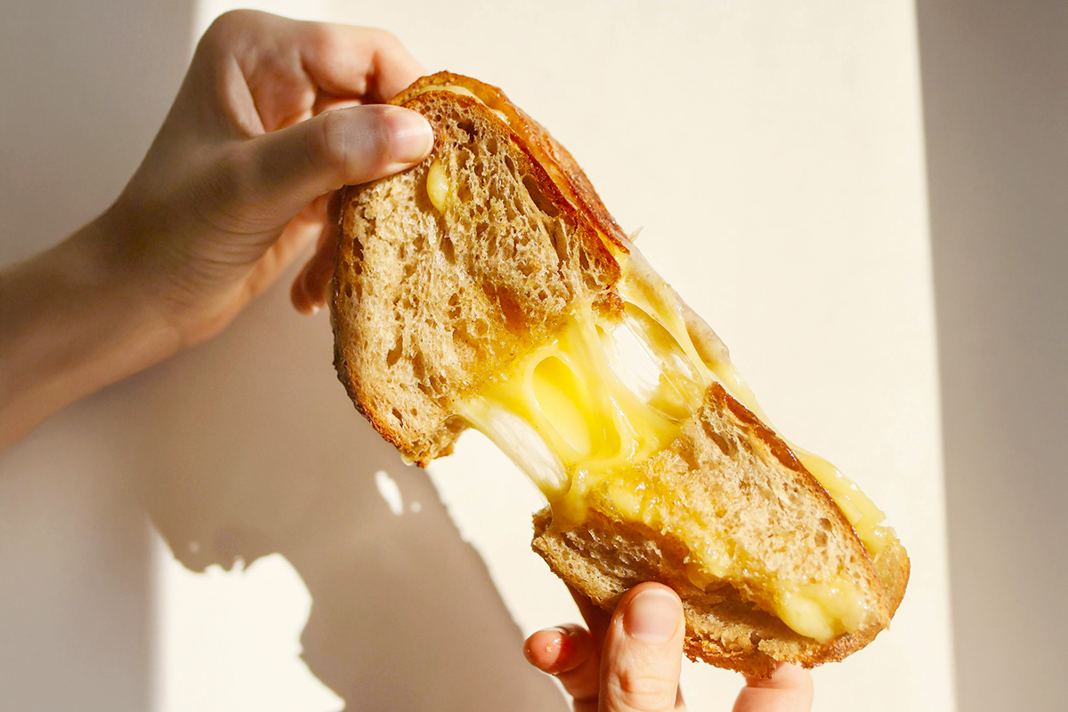 Anonymous person pulling apart a grilled cheese with their hands, showcasing the gooeyness of the melted American cheese.
