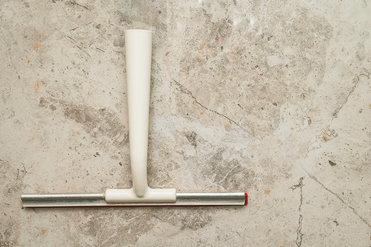 A squeegee with a white plastic handle on a flat marble surface, photographed from above.