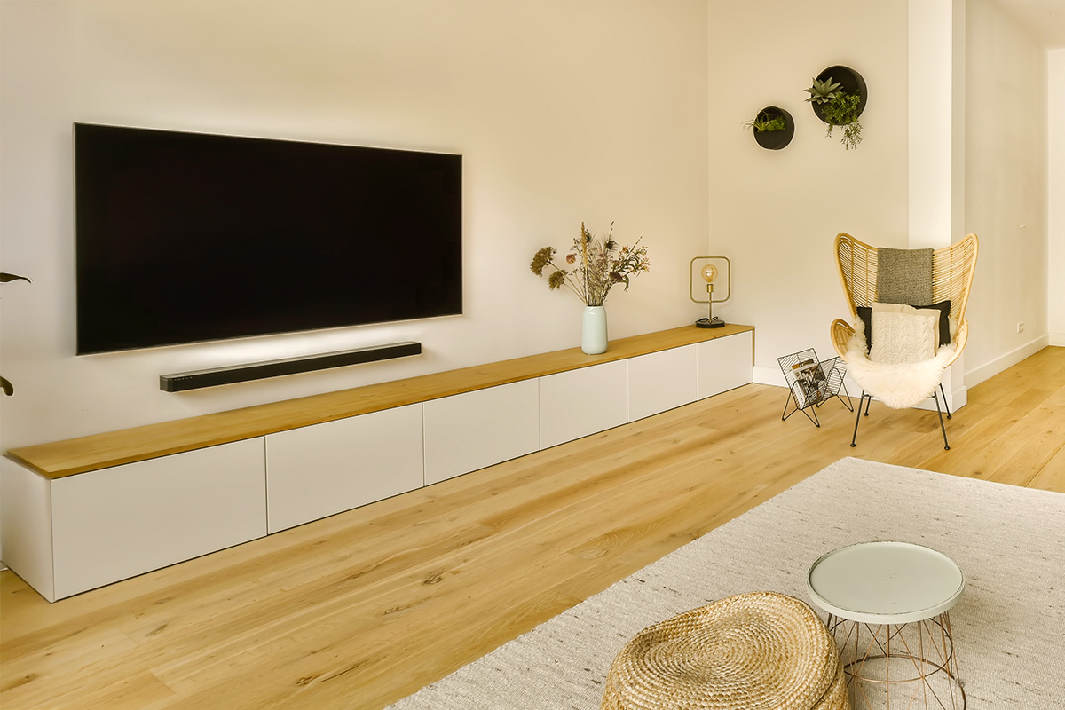 A wall-mounted TV over an extra-long media console with a wood top and white closed storage.