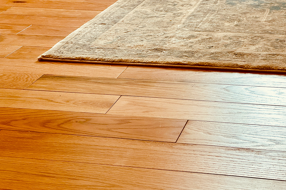 Close up of yellow-y oak hardwood floors with a beige area rug in the top right corner.