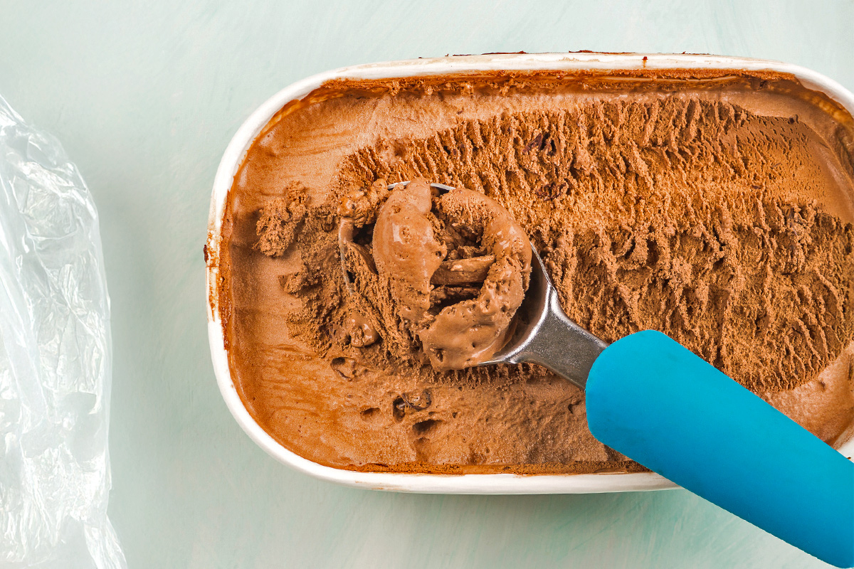 Someone using a blue ice cream scooper to scoop chocolate ice cream out of a tub.