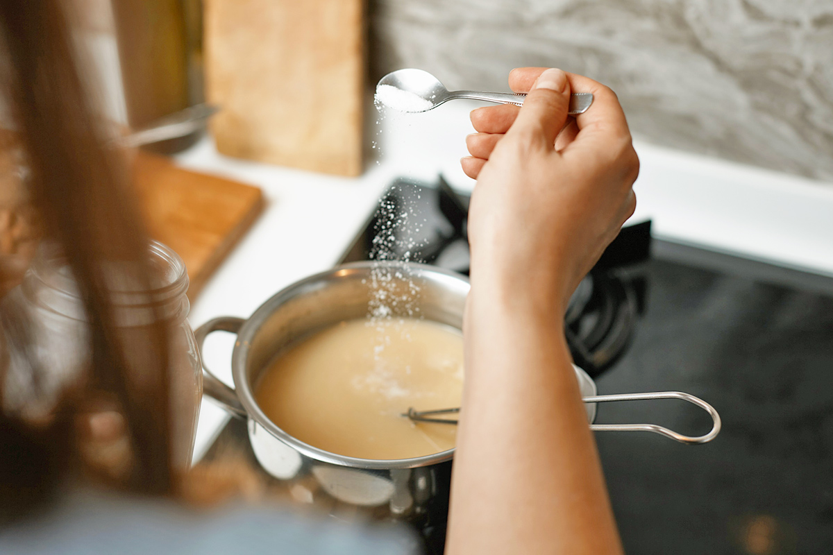 Over-the-shoulder shot of a woman adding salt to a saucepan of brown gravy.
