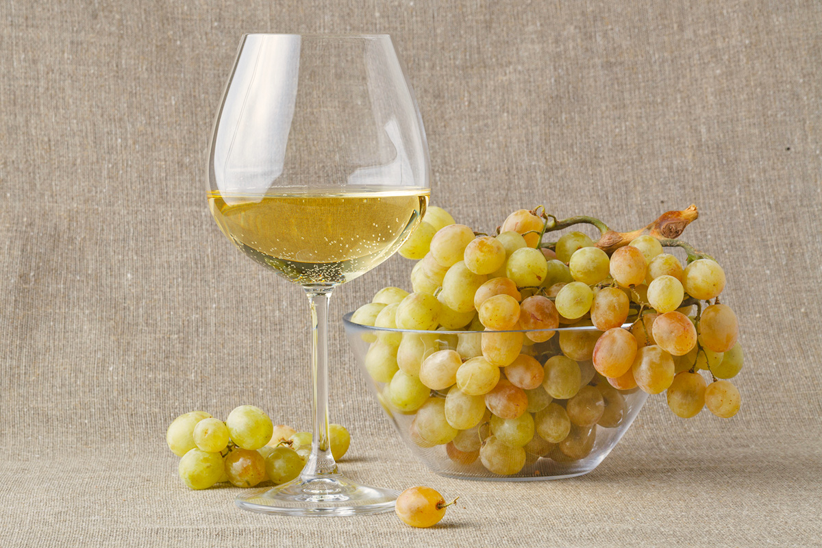 A glass of white wine next to a glass bowl of green grapes.