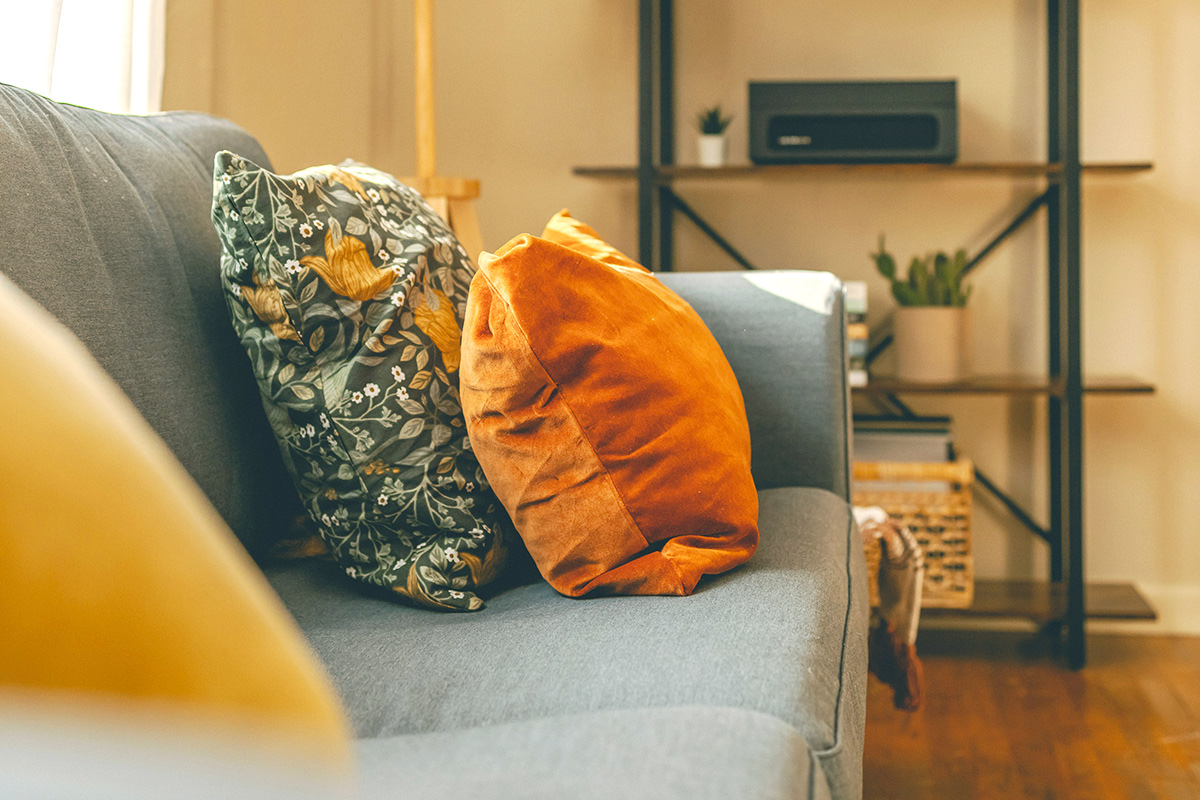 Two in-focus throw pillows on a gray couch. One is orange velvet, and the other is teal with a botanical print.