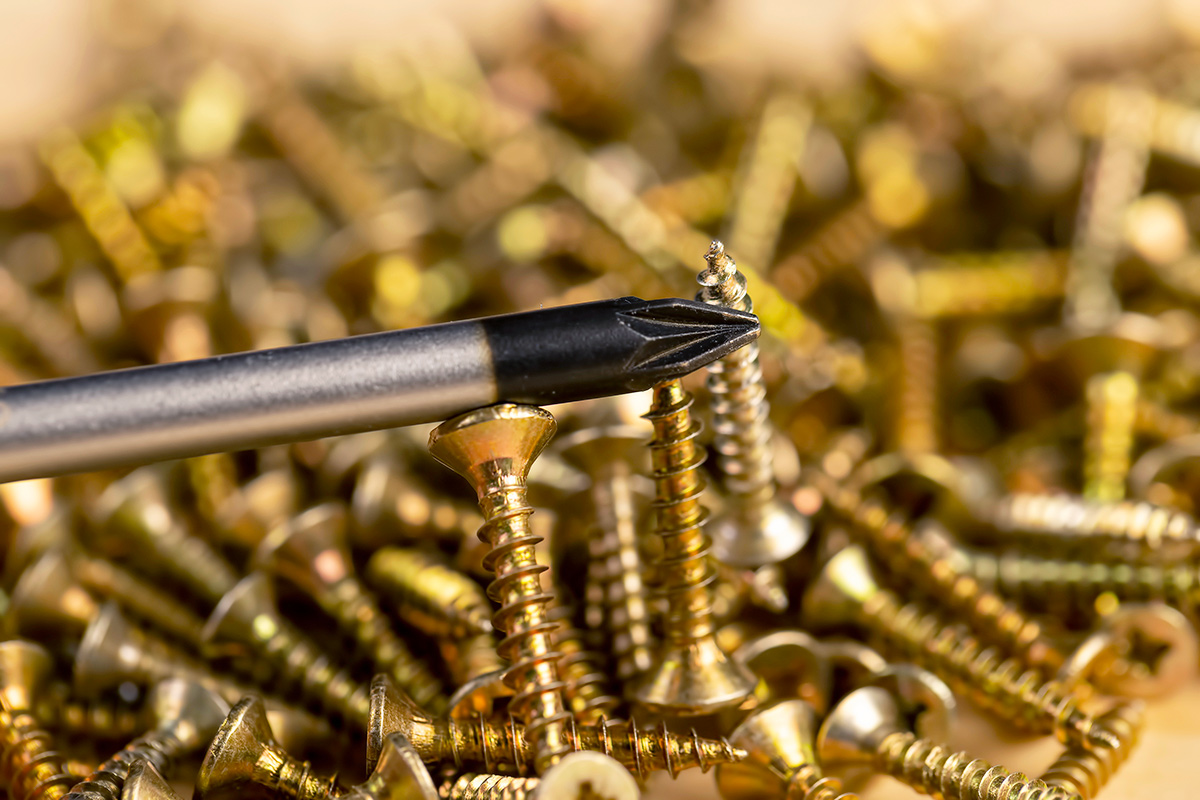 Close-up of a magnetized tip of a screwdriver picking up a gold screw in a large pile of them.