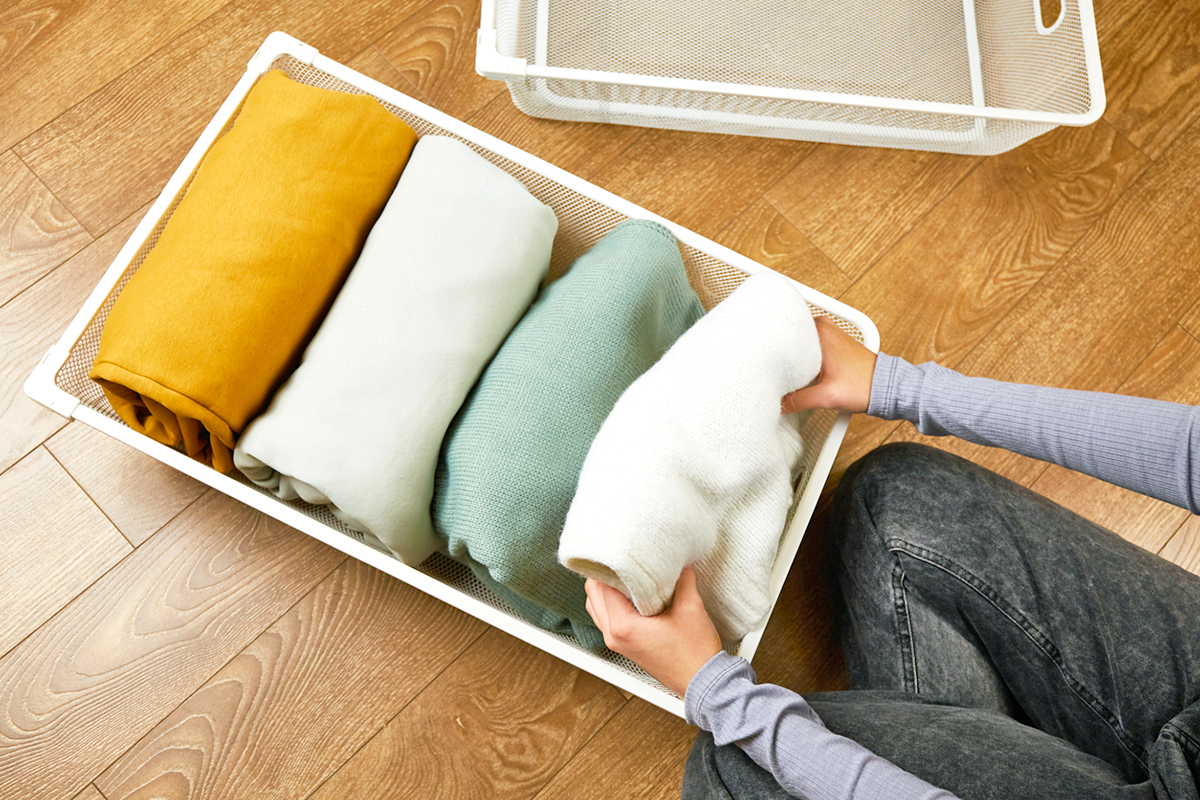 Anonymous woman file-folding bulky sweaters into an organizing bin on the floor.