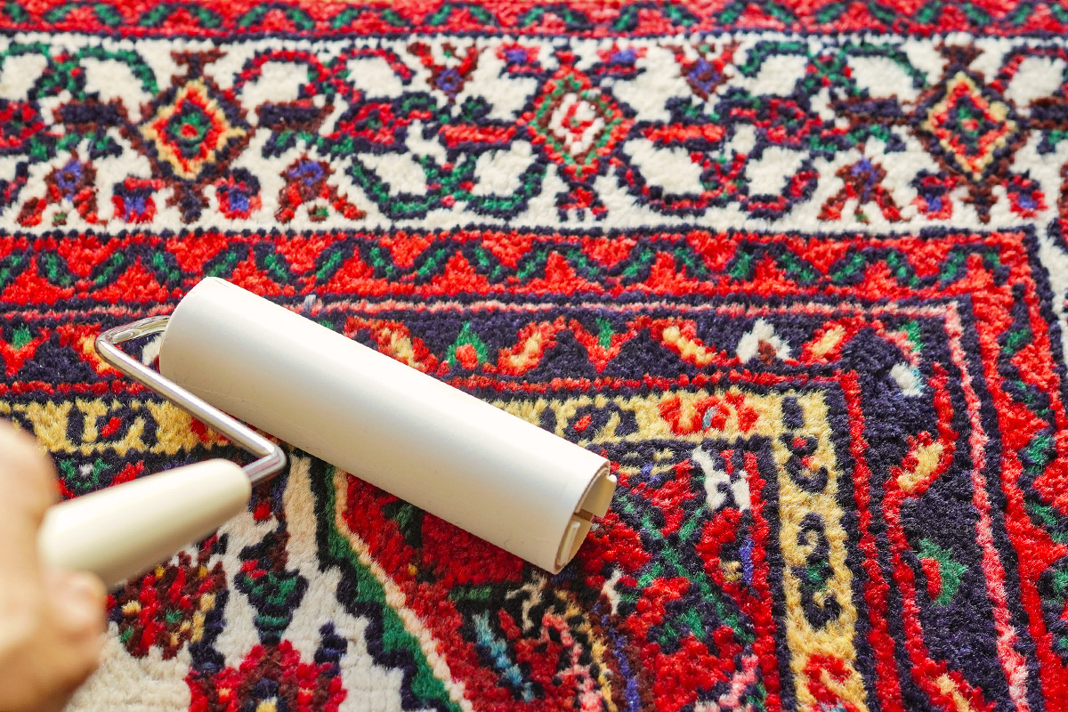 Anonymous person using a lint roller to clean a vibrant, patterned area rug.