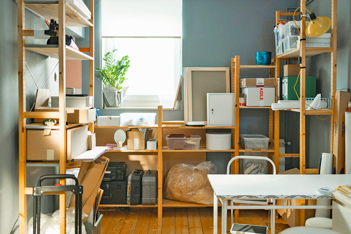 A small room painted blue with a bunch of open shelves for holding random items, including boxes, briefcases, and packing materials.