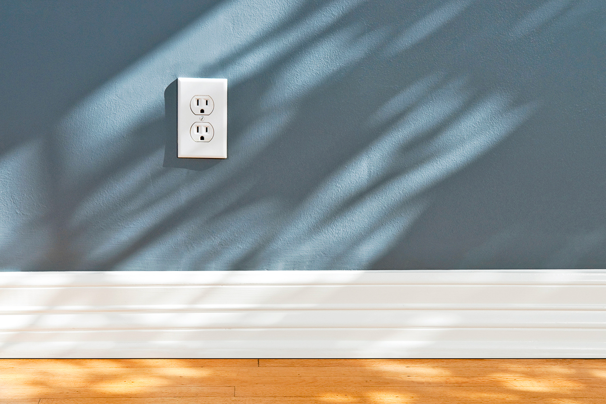 A blue wall with white baseboards and a wood floor with light cascading across it.