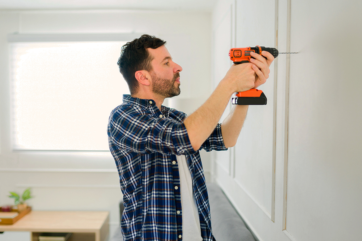 A man in a plaid shirt drilling into the wall with a power drill.