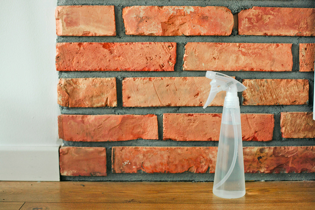 A clear spray bottle on a wooden floor in front of a brick wall.