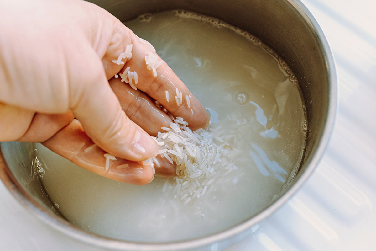Person washing white rice in a metal bowl of water.
