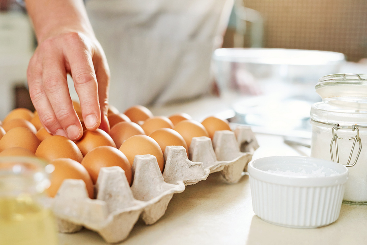 Anonymous person taking an egg out of an open carton. There are baking supplies in the background.