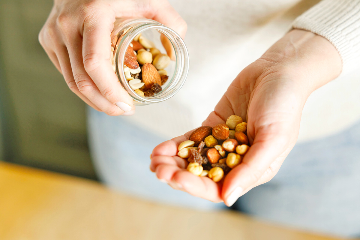 Anonymous woman pouring herself a handful of mixed nuts from a glass Mason jar.