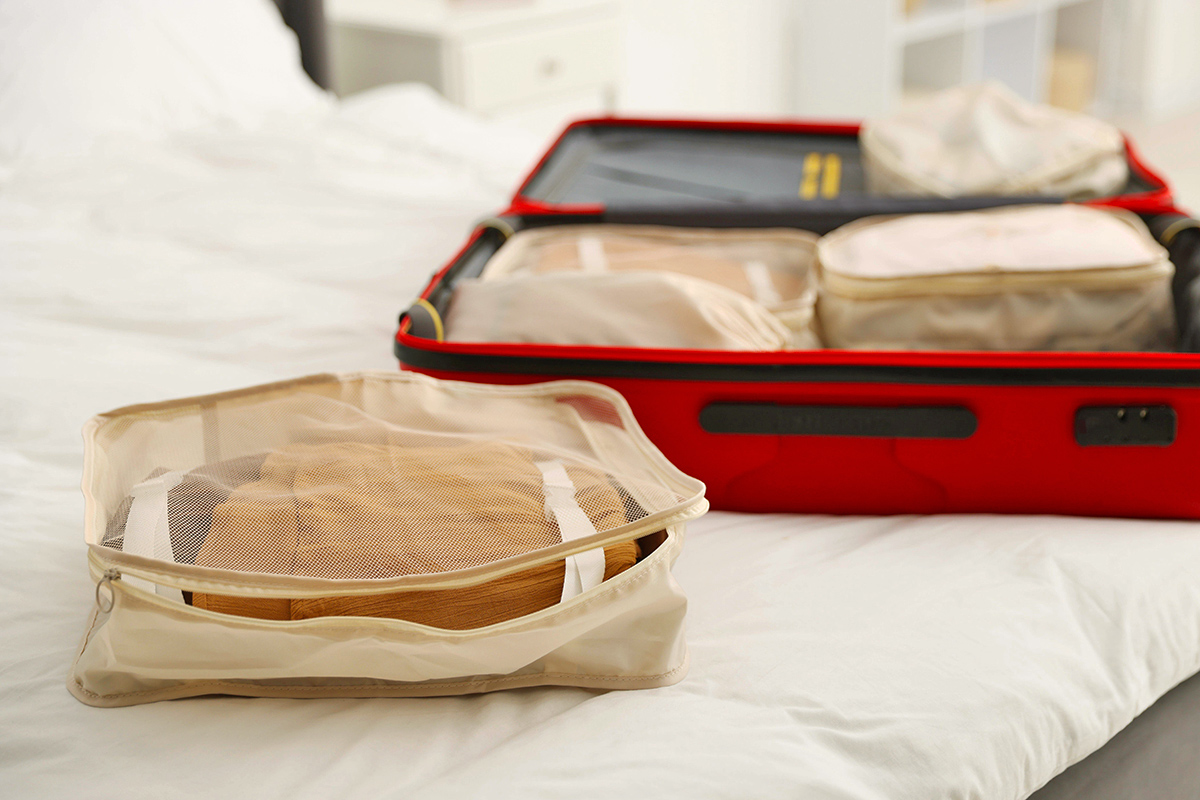 Packing cubes on a bed next to an open red suitcase.