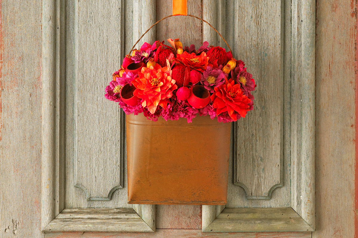 Close-up of a front door with a copper-colored metal basket filled with red and pink artificial flowers.