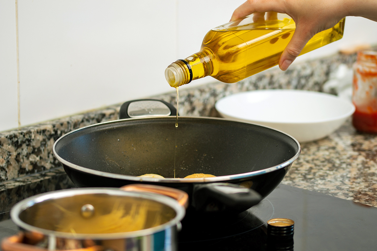 Anonymous person pouring oil into a wok on an electric cooktop.