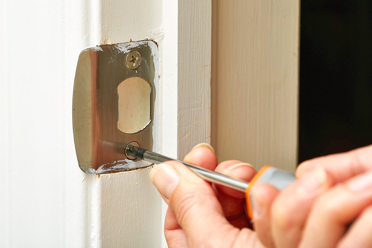 Anonymous person using a screwdriver to adjust the strike plate in a door frame.