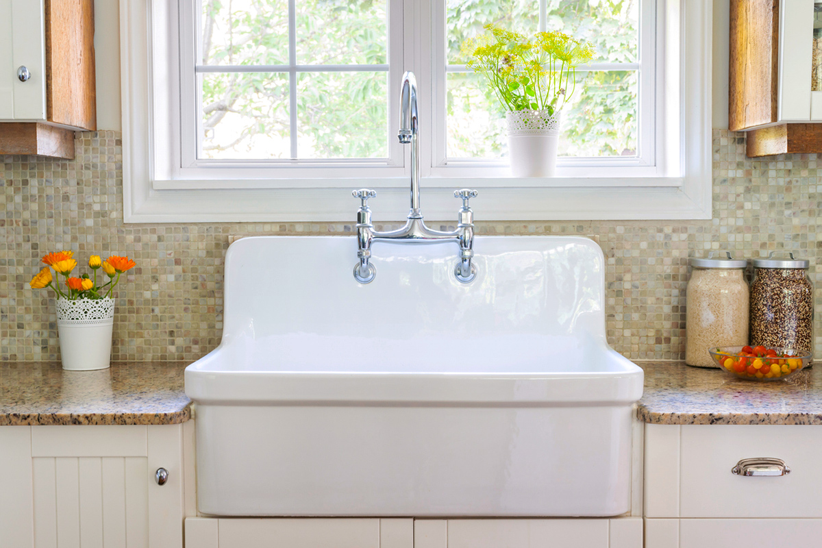 A large, apron-front porcelain sink with a chrome bridge faucet.