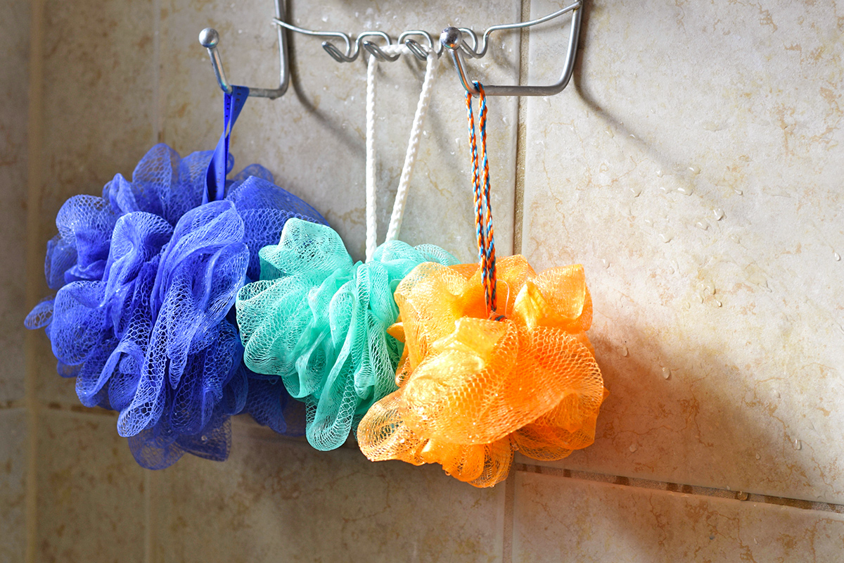 Purple, turquoise, and orange mesh poufs hang from a silver rack in a tile shower.