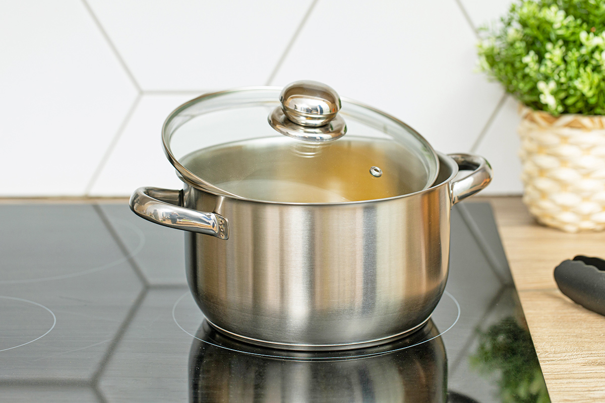 A stainless steel pot on an electric cooktop with the lid partially on.