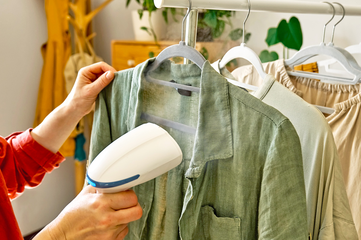 Anonymous person steaming a button-down green linen shirt on a hanger.