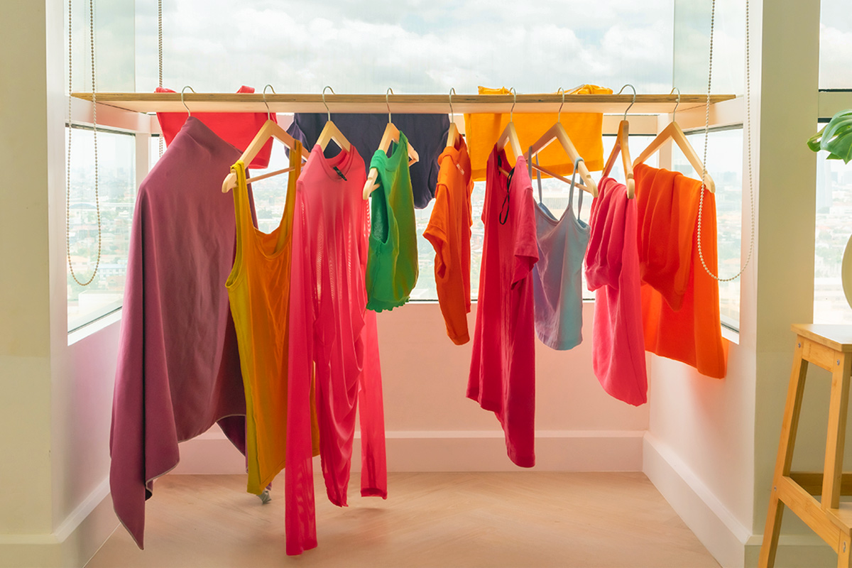 Colorful items of clothing on wooden hangers hanging off of a board in a high-rise condo with lots of windows.