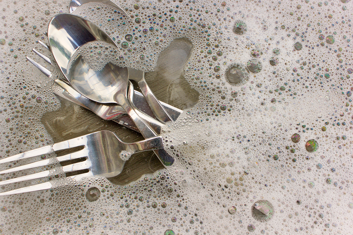 Silverware partially submerged in soapy water.