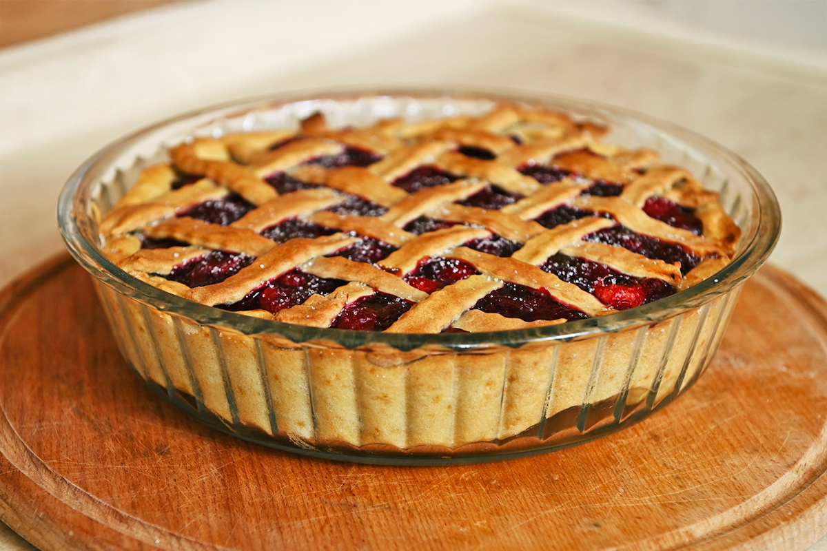 A cherry pie with a lattice crust in a glass baking dish on a wooden trivet.