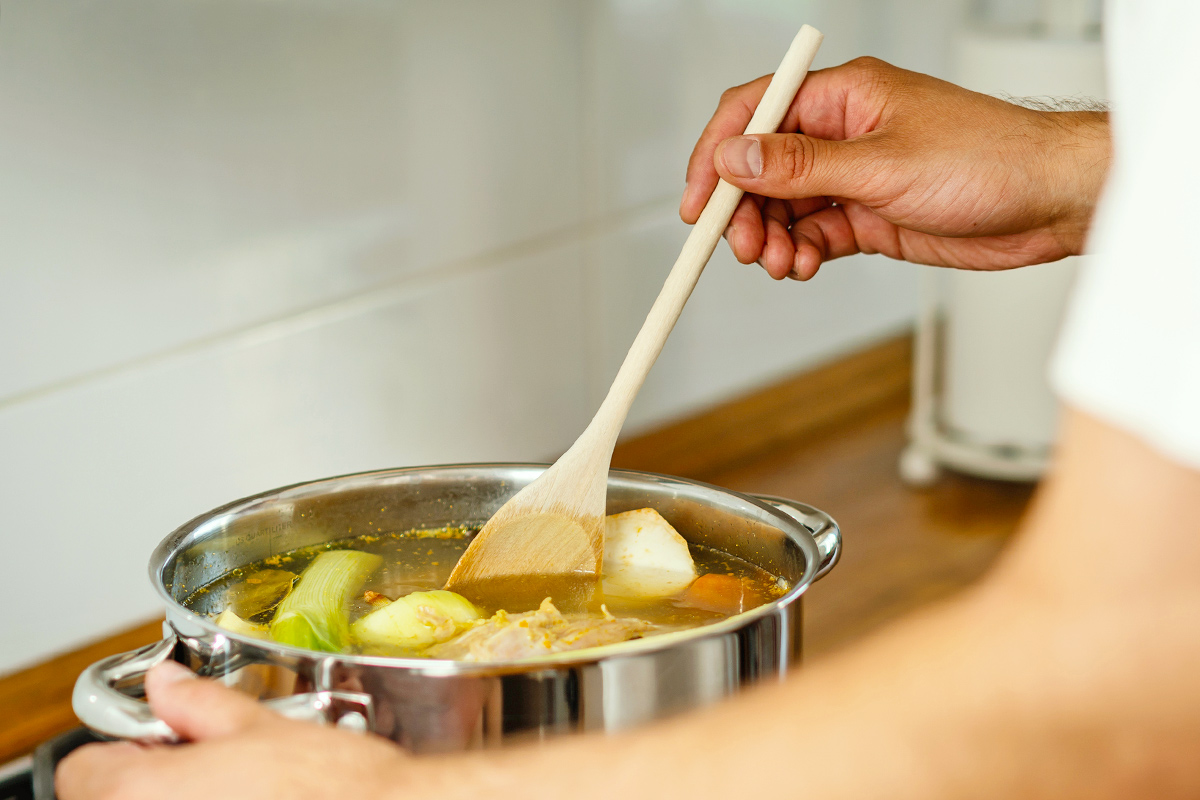 Anonymous person making a pot of vegetable stock on the stove. They are using a wooden spoon to stir it.