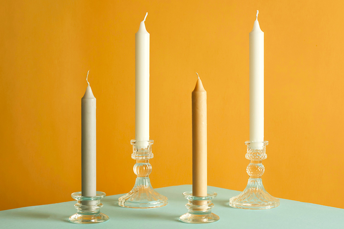 Four plain taper candles in glass holders against a dark yellow background.